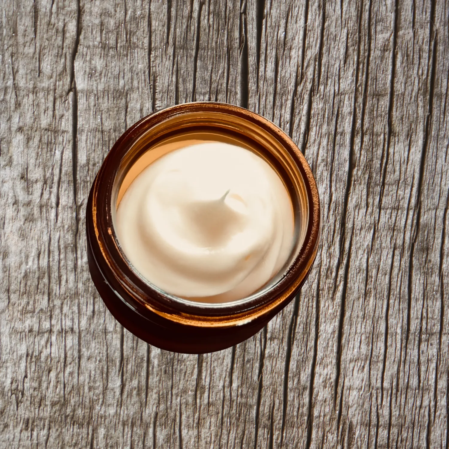 An open jar of bison tallow cream on weathered wood
